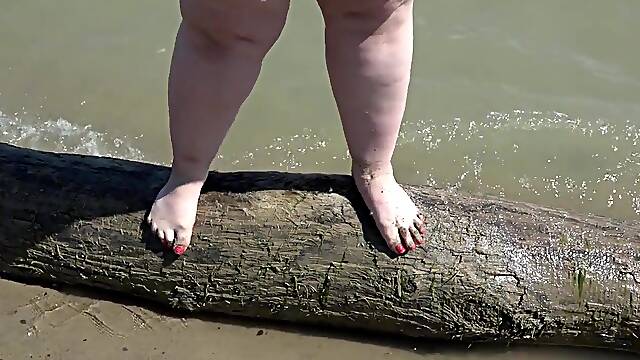 A obese woman with large feet walks along the shore.